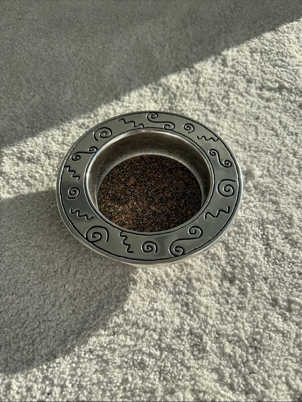 Silver wine bottle coaster with decorative swirl rim.